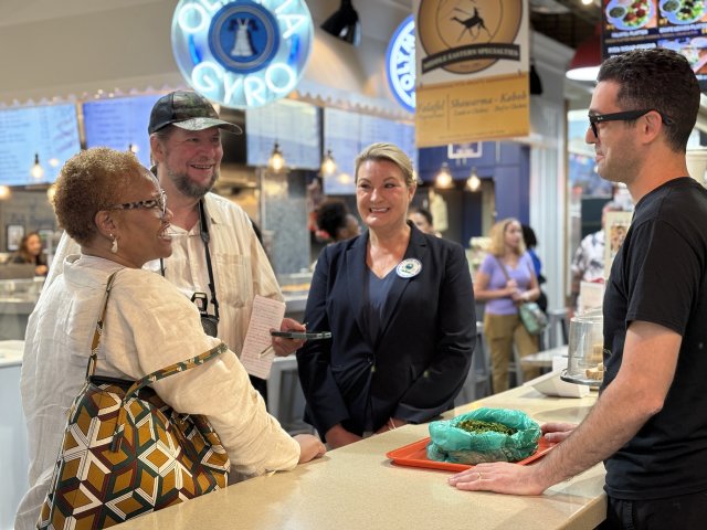 Three people gathered around counter of food service area for Komal's food stand at Reading Terminal Market