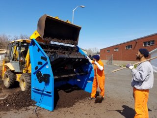 Image of a group of inmates filling a bin with compost. 