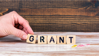 A hand places a letter g tile in the line of wooden letter tiles spelling grant