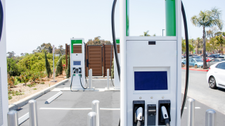 A white EV charging station with green accent in the foreground with more chargers in the background