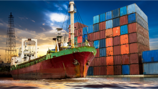 Freighter ship with multiple colors of containers stacked in background against a night sky.