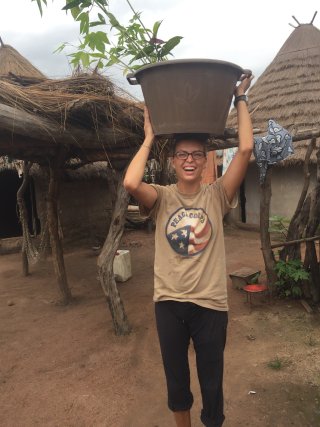 Claire Brisse holds a large bucket over her head in a village in Senegal