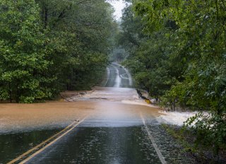 A road with flowing stormwater across it, blocking passage.