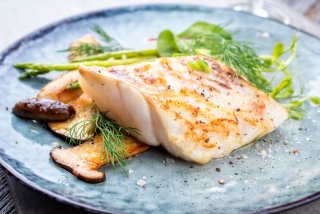 Fried cod fish filet with green asparagus and mushrooms as close up on a plate.