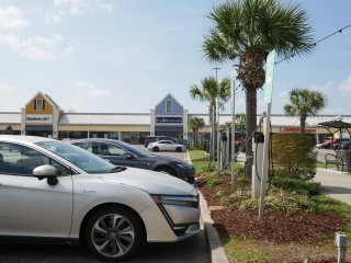 The image shows cars parked next to an Electric Vehicle charger in a shopping center