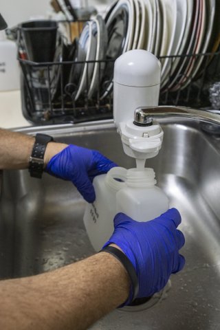 A scientist fills up two containers with water from a kitchen faucet for sampling.