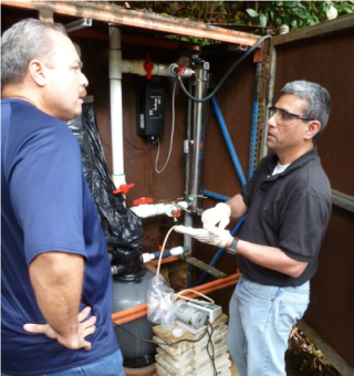 Two people standing next to each other with drinking water treatment systems with pipes in the background.