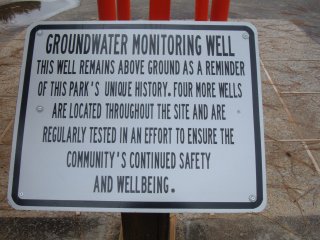 Sign that reads: Groundwater monitoring well. This well remains above ground as a reminder of this park's unique history. Four more wells are located throughout the site and are regularly tested in an effort to ensure the community's continued safety and wellbeing.