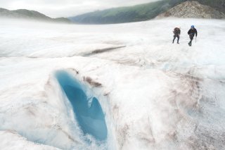 Hikers on a glacier with melted glacial water in a shallow pool nearby