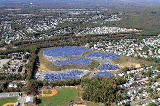 An aerial view of a solar array installation surrounded by residential homes and a baseball field.