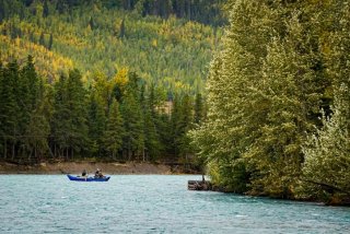 scenic image of a river or lake with a small boat on it surrounded by green forest