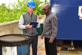 Two men with tablet next to a drum and a trash roll off container