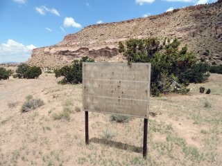 Desert landscape with a large, faded sign that reads "Potential Radiological Hazard Below Service"
