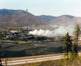 Smoke billowing from multiple stacks within a large open mining complex.