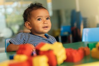 A baby sits at a table playing with blocks