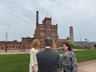 Three people have a conversation in front of a brownfields site. 