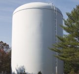 white storage tank for dinking water surrounded by trees and a blue sky.