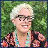 A woman with short, curly blonde hair and dark rimmed glasses.