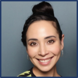 A woman with dark hair in a high bun and silver hoop earrings. She is smiling.