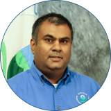 Speaker Jatin has dark hair and is wearing a blue collared shirt while standing in front of the EPA flag and a grey background.