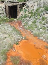 An adit entrance with orange metal contamination seeping out downhill.